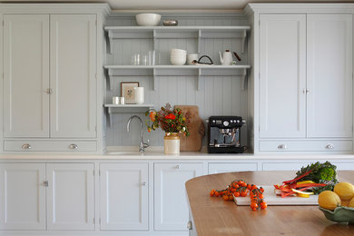 Klassisk inredning av ett kök med öppen planlösning, med en undermonterad diskho, marmorbänkskiva, vitt stänkskydd, stänkskydd i marmor, svarta vitvaror, kalkstensgolv och en köksö