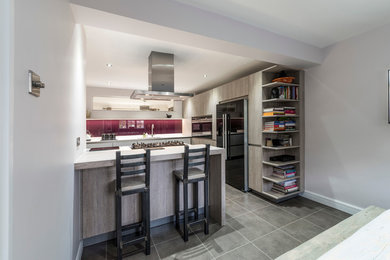 Medium sized contemporary l-shaped kitchen/diner in Manchester with an integrated sink, flat-panel cabinets, white cabinets, quartz worktops, red splashback, glass sheet splashback, black appliances, vinyl flooring and a breakfast bar.