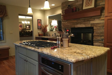 Exempel på ett mellanstort klassiskt kök, med en dubbel diskho, luckor med upphöjd panel, skåp i mellenmörkt trä, granitbänkskiva, beige stänkskydd, stänkskydd i stenkakel, rostfria vitvaror, mellanmörkt trägolv och en köksö