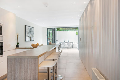 Eat-in kitchen - mid-sized modern galley cement tile floor and black floor eat-in kitchen idea in London with a drop-in sink, flat-panel cabinets, medium tone wood cabinets, wood countertops, multicolored backsplash, ceramic backsplash, white appliances and an island