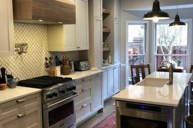 Inspiration for a mid-sized farmhouse u-shaped dark wood floor and brown floor eat-in kitchen remodel in Atlanta with a farmhouse sink, recessed-panel cabinets, white cabinets, quartzite countertops, white backsplash, ceramic backsplash, stainless steel appliances, an island and white countertops