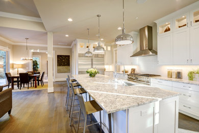 Mid-sized trendy l-shaped medium tone wood floor and brown floor open concept kitchen photo in Los Angeles with an undermount sink, shaker cabinets, white cabinets, granite countertops, white backsplash, subway tile backsplash, stainless steel appliances, an island and gray countertops