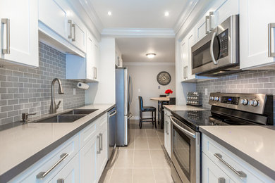Small classic galley kitchen in Toronto with a double-bowl sink, shaker cabinets, white cabinets, quartz worktops, grey splashback, metro tiled splashback, stainless steel appliances and ceramic flooring.