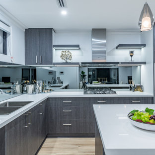 This is an example of a contemporary l-shaped kitchen in Perth with a double-bowl sink, flat-panel cabinets, grey cabinets, mirror splashback, black appliances, light hardwood floors, with island, beige floor and white benchtop.