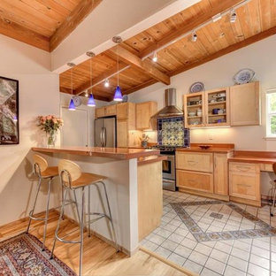 Modelo de cocina lineal, mediterránea, de tamaño medio, cerrada, con armarios estilo shaker, puertas de armario de madera clara, encimera de cuarzo compacto, salpicadero multicolor, salpicadero de azulejos de cemento, electrodomésticos de acero inoxidable, suelo de baldosas de porcelana, península, suelo gris y encimeras naranjas