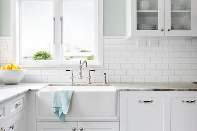 Inspiration for a mid-sized timeless u-shaped porcelain tile kitchen remodel in Auckland with a farmhouse sink, recessed-panel cabinets, white cabinets, granite countertops, white backsplash, stainless steel appliances and subway tile backsplash