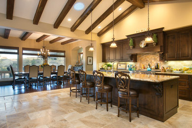 Inspiration for a large timeless travertine floor and beige floor eat-in kitchen remodel in San Diego with an undermount sink, raised-panel cabinets, dark wood cabinets, beige backsplash, stainless steel appliances and an island