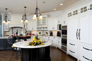 Example of a classic l-shaped dark wood floor kitchen design in New York with recessed-panel cabinets, white cabinets, beige backsplash, subway tile backsplash, stainless steel appliances and an island