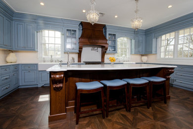 Large elegant u-shaped dark wood floor and brown floor eat-in kitchen photo in New York with a farmhouse sink, recessed-panel cabinets, blue cabinets, solid surface countertops, white backsplash, ceramic backsplash, an island and paneled appliances