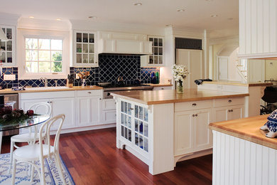 Example of a large farmhouse single-wall dark wood floor eat-in kitchen design in New York with a drop-in sink, shaker cabinets, white cabinets, wood countertops, blue backsplash, porcelain backsplash, paneled appliances and an island