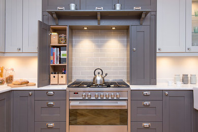 Example of a mid-sized arts and crafts u-shaped light wood floor kitchen design in Other with a farmhouse sink, shaker cabinets, gray cabinets, solid surface countertops, gray backsplash, stainless steel appliances and subway tile backsplash