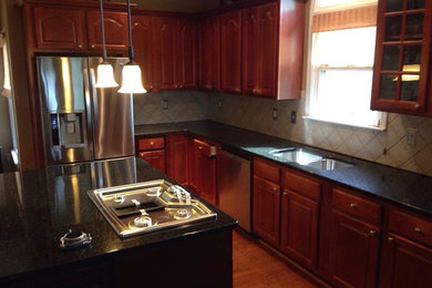 Mid-sized elegant l-shaped dark wood floor and brown floor enclosed kitchen photo in Birmingham with a double-bowl sink, raised-panel cabinets, dark wood cabinets, granite countertops, beige backsplash, ceramic backsplash, stainless steel appliances and an island