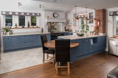 Classic u-shaped kitchen in Other with a belfast sink, raised-panel cabinets, blue cabinets, black appliances, a breakfast bar and grey floors.
