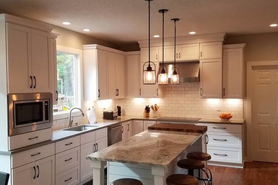 Design ideas for a large traditional l-shaped enclosed kitchen in Other with shaker cabinets, white cabinets, composite countertops, white splashback, metro tiled splashback, stainless steel appliances, dark hardwood flooring, an island and brown floors.