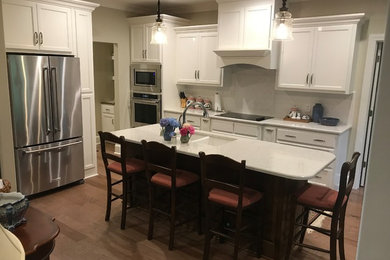 Mid-sized elegant l-shaped dark wood floor and brown floor open concept kitchen photo in Other with a double-bowl sink, recessed-panel cabinets, white cabinets, white backsplash, subway tile backsplash, stainless steel appliances, an island and white countertops