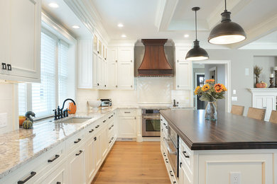 Inspiration for a large timeless l-shaped light wood floor open concept kitchen remodel in Boston with an undermount sink, recessed-panel cabinets, white cabinets, granite countertops, white backsplash, ceramic backsplash, stainless steel appliances and an island