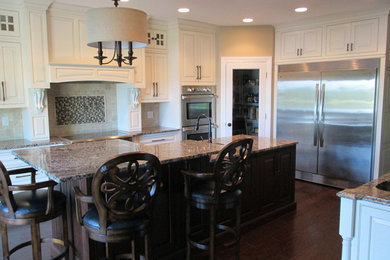 Example of a large classic dark wood floor open concept kitchen design in Cincinnati with an undermount sink, beaded inset cabinets, white cabinets, granite countertops, beige backsplash, stone tile backsplash, stainless steel appliances and two islands