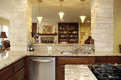Open concept kitchen - mid-sized traditional u-shaped travertine floor open concept kitchen idea in Austin with a double-bowl sink, raised-panel cabinets, granite countertops, multicolored backsplash, stainless steel appliances, an island, medium tone wood cabinets and glass tile backsplash