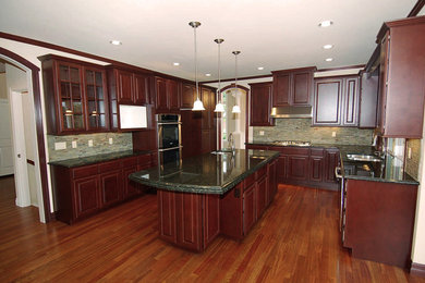 Large elegant u-shaped medium tone wood floor and brown floor eat-in kitchen photo in Houston with a double-bowl sink, raised-panel cabinets, dark wood cabinets, granite countertops, gray backsplash, matchstick tile backsplash, stainless steel appliances and an island
