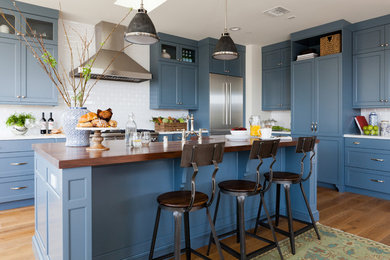Example of a large classic medium tone wood floor kitchen design in Los Angeles with a farmhouse sink, recessed-panel cabinets, blue cabinets, wood countertops, white backsplash, subway tile backsplash, stainless steel appliances and an island