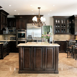 Exemple d'une cuisine chic en L de taille moyenne et fermée avec un îlot central, un placard avec porte à panneau surélevé, des portes de placard en bois sombre, un plan de travail en granite, une crédence beige, une crédence en mosaïque, un électroménager en acier inoxydable, un évier encastré et un sol en travertin.
