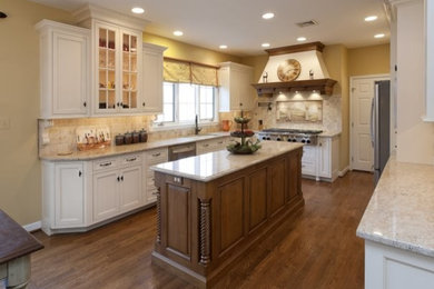 Example of a large classic u-shaped medium tone wood floor and brown floor enclosed kitchen design in Philadelphia with an undermount sink, recessed-panel cabinets, white cabinets, granite countertops, beige backsplash, travertine backsplash, stainless steel appliances, an island and beige countertops