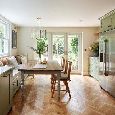 Example of a large classic u-shaped medium tone wood floor and brown floor eat-in kitchen design in London with a farmhouse sink, shaker cabinets, green cabinets, quartzite countertops, white backsplash, ceramic backsplash, stainless steel appliances, no island and multicolored countertops