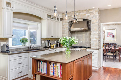 Mid-sized elegant l-shaped medium tone wood floor and beige floor enclosed kitchen photo in Orange County with stainless steel appliances, an island, a drop-in sink, raised-panel cabinets, white cabinets, gray backsplash and subway tile backsplash