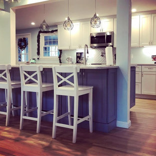 This is an example of a mid-sized traditional galley open plan kitchen in Boston with white cabinets, white splashback, ceramic splashback, stainless steel appliances, light hardwood floors, a peninsula, beige floor, grey benchtop and recessed-panel cabinets.