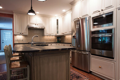 Ejemplo de cocina tradicional con puertas de armario grises, salpicadero beige, electrodomésticos de acero inoxidable, suelo de madera en tonos medios y una isla