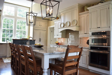 Exempel på ett avskilt, stort klassiskt u-kök, med en dubbel diskho, luckor med upphöjd panel, beige skåp, granitbänkskiva, beige stänkskydd, stänkskydd i glaskakel, rostfria vitvaror, mellanmörkt trägolv, en köksö och brunt golv