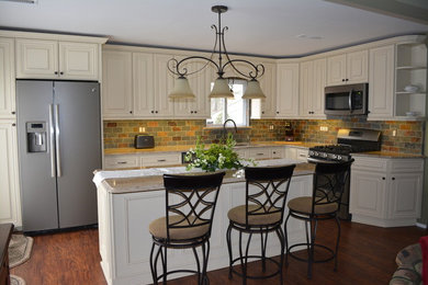Example of a mid-sized classic l-shaped laminate floor eat-in kitchen design in Philadelphia with a double-bowl sink, raised-panel cabinets, white cabinets, granite countertops, multicolored backsplash, stone tile backsplash, stainless steel appliances and an island