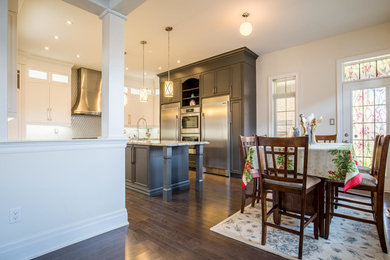 Enclosed kitchen - mid-sized traditional u-shaped dark wood floor enclosed kitchen idea in Toronto with a farmhouse sink, shaker cabinets, white cabinets, quartz countertops, white backsplash, glass tile backsplash, stainless steel appliances and an island