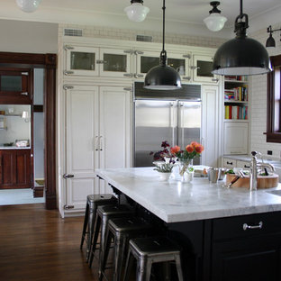 Inspiration for a timeless kitchen remodel in Chicago with glass-front cabinets, subway tile backsplash, a farmhouse sink, white cabinets, white backsplash, stainless steel appliances and marble countertops