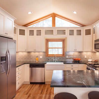 Elegant u-shaped kitchen photo in Denver with glass-front cabinets, stainless steel appliances, subway tile backsplash, a farmhouse sink and soapstone countertops