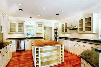 Large elegant u-shaped dark wood floor and red floor enclosed kitchen photo in Boston with recessed-panel cabinets, white cabinets, stainless steel appliances, an island and black countertops