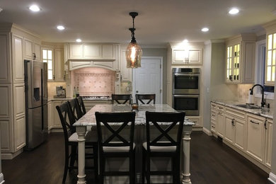 Example of a mid-sized classic u-shaped dark wood floor eat-in kitchen design in New York with an undermount sink, raised-panel cabinets, white cabinets, quartz countertops, beige backsplash, ceramic backsplash, stainless steel appliances and an island