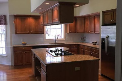 Mid-sized elegant l-shaped medium tone wood floor and brown floor open concept kitchen photo in Cleveland with a double-bowl sink, raised-panel cabinets, medium tone wood cabinets, granite countertops, white backsplash, porcelain backsplash, stainless steel appliances and an island