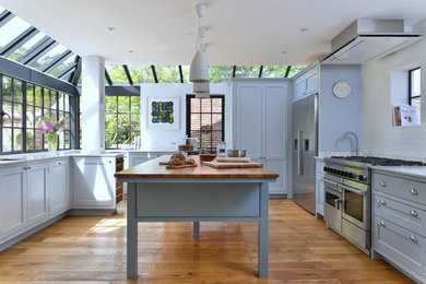 Inspiration for a traditional u-shaped kitchen in London with a submerged sink, beaded cabinets, grey cabinets, white splashback, stainless steel appliances, medium hardwood flooring and an island.