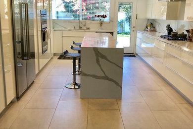Inspiration for a large contemporary u-shaped porcelain tile and beige floor kitchen remodel in Los Angeles with an undermount sink, flat-panel cabinets, white cabinets, quartzite countertops, gray backsplash, stone slab backsplash, stainless steel appliances and an island