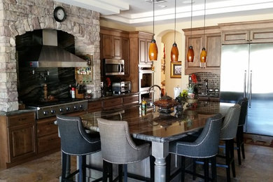 Inspiration for a large timeless l-shaped travertine floor eat-in kitchen remodel in Phoenix with an undermount sink, raised-panel cabinets, gray cabinets, granite countertops, black backsplash, stone slab backsplash, stainless steel appliances and an island