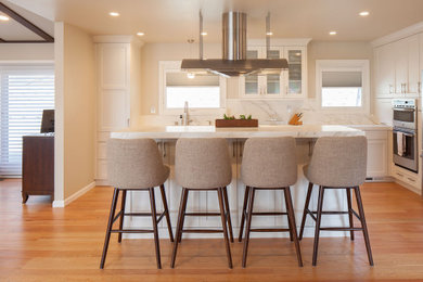 Mid-sized elegant l-shaped medium tone wood floor and brown floor eat-in kitchen photo in San Francisco with shaker cabinets, white cabinets, quartz countertops, white backsplash, quartz backsplash, stainless steel appliances, an island and white countertops
