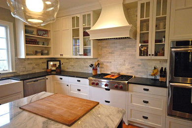Inspiration for a mid-sized timeless l-shaped medium tone wood floor eat-in kitchen remodel in Charlotte with a farmhouse sink, recessed-panel cabinets, white cabinets, marble countertops, white backsplash, stone tile backsplash, stainless steel appliances and an island