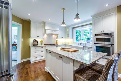 Photo of a medium sized traditional l-shaped kitchen/diner in Toronto with beaded cabinets, white cabinets, granite worktops, white splashback, metro tiled splashback, stainless steel appliances, an island, a belfast sink, dark hardwood flooring and brown floors.