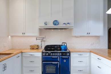 Klassisk inredning av ett stort kök, med en dubbel diskho, luckor med infälld panel, vita skåp, träbänkskiva, vitt stänkskydd, stänkskydd i metallkakel, färgglada vitvaror, mörkt trägolv, en halv köksö och brunt golv