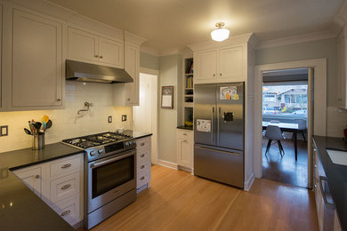 Foto på ett avskilt, mellanstort amerikanskt l-kök, med en undermonterad diskho, skåp i shakerstil, vita skåp, bänkskiva i kvarts, vitt stänkskydd, stänkskydd i keramik, rostfria vitvaror, ljust trägolv och brunt golv