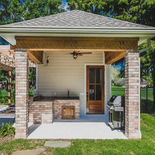 Small traditional l-shaped eat-in kitchen in New Orleans with an undermount sink, louvered cabinets, medium wood cabinets, granite benchtops, beige splashback, stone slab splashback, stainless steel appliances, concrete floors and with island.