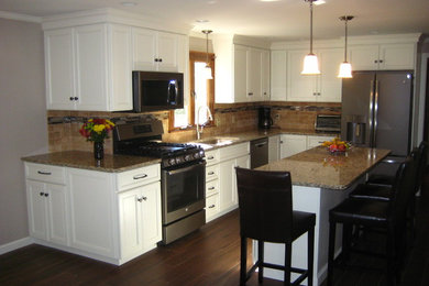 Example of a mid-sized classic l-shaped dark wood floor and brown floor kitchen design in Boston with an undermount sink, recessed-panel cabinets, white cabinets, granite countertops, brown backsplash, stone tile backsplash, stainless steel appliances and an island