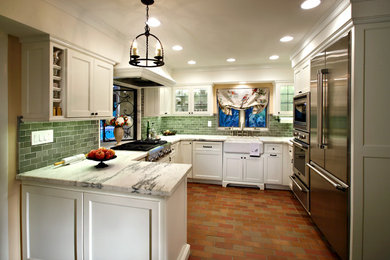 Inspiration for a mid-sized farmhouse u-shaped brick floor and red floor kitchen remodel in Phoenix with a farmhouse sink, shaker cabinets, white cabinets, green backsplash, subway tile backsplash, stainless steel appliances and a peninsula
