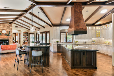 Example of a tuscan u-shaped medium tone wood floor open concept kitchen design in Phoenix with raised-panel cabinets, white cabinets, beige backsplash, mosaic tile backsplash, stainless steel appliances and two islands
